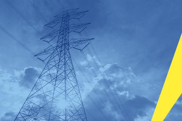 The photograph is taken from the ground looking up. It show and electricity pylon, with sunshine and clouds in the background